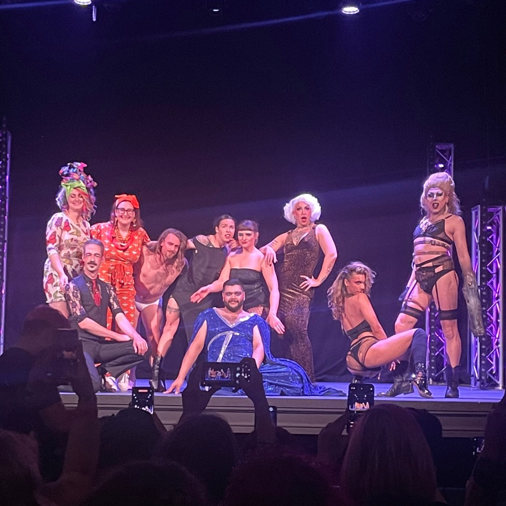 A group of burlesque performers posing on stage during a show, showcasing a variety of costumes and styles under stage lights.